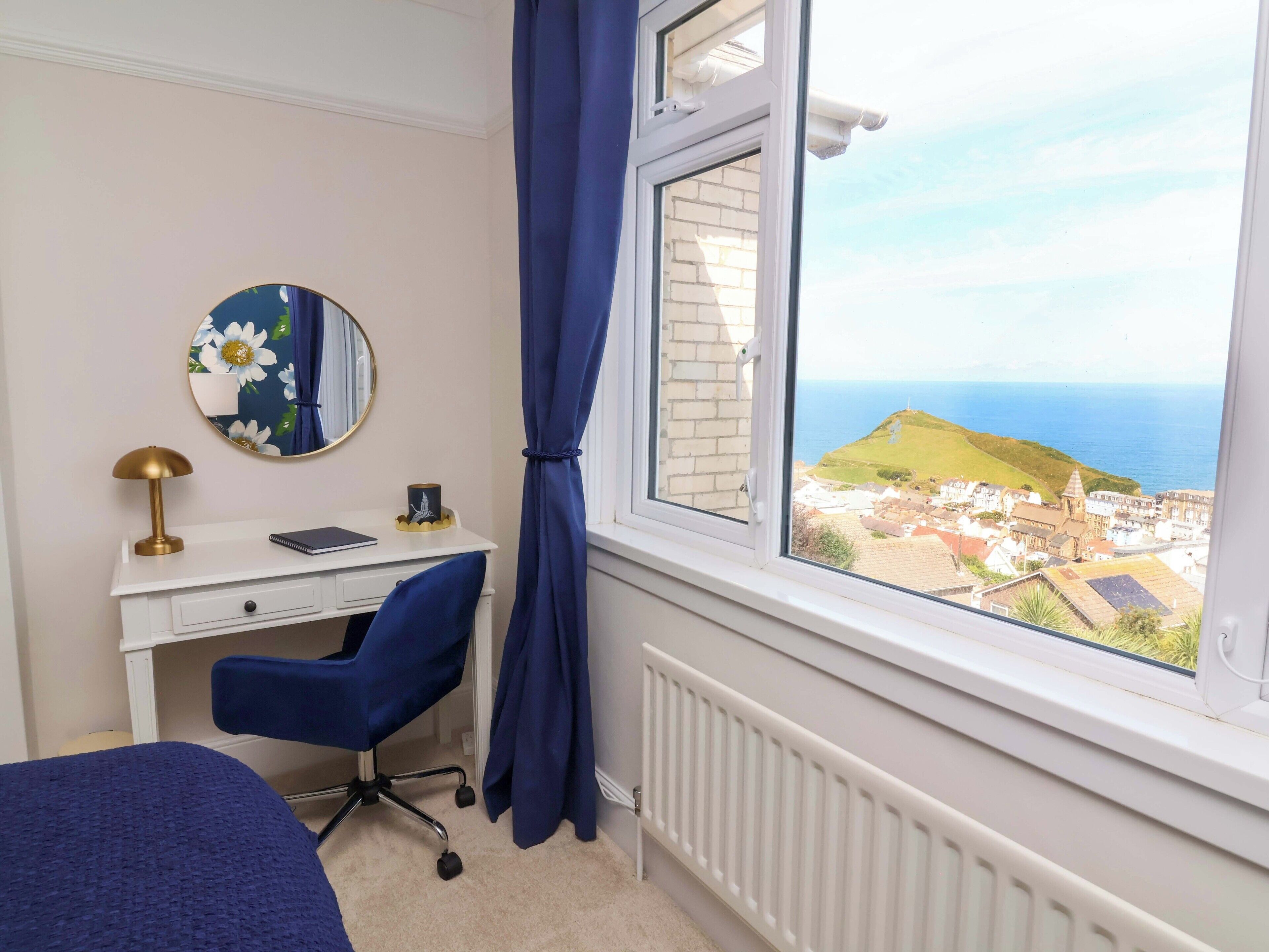 Une chambre avec un bureau, une chaise et une vue sur une ville côtière.