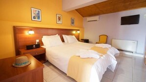 A hotel room with a wooden headboard, a bed with white linens, a nightstand, a bedside table with a hat, and a wall-mounted TV. - Mirabel CityCenter Hotel (Argostolion)