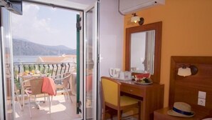 A hotel room with a balcony, a desk with a chair, a bed, and a nightstand with a lamp and a hat. - Mirabel CityCenter Hotel (Argostolion)
