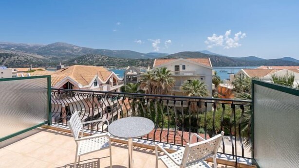 A balcony with a table and chairs, overlooking a coastal area with buildings and mountains. - Mirabel CityCenter Hotel (Argostolion)