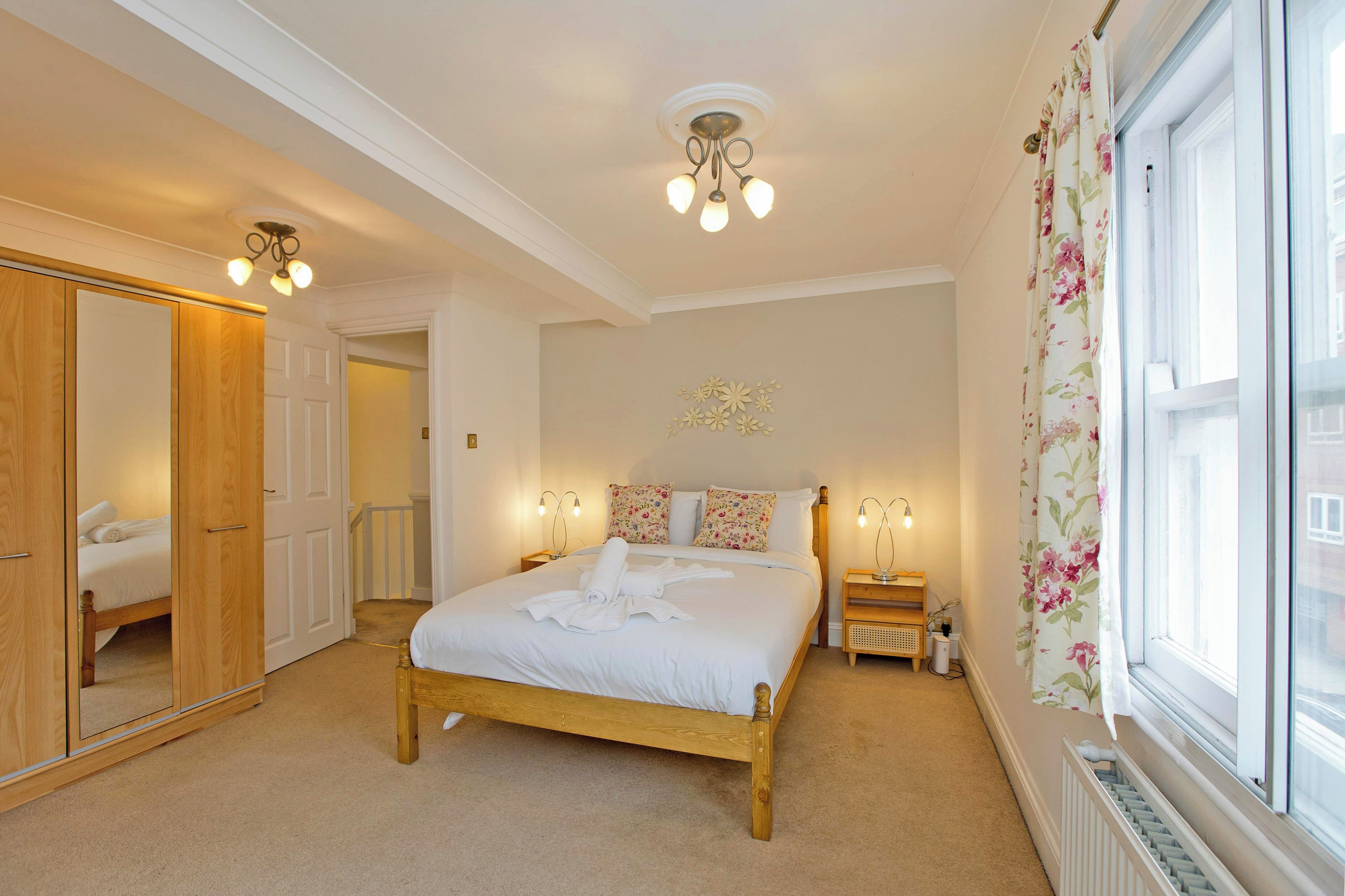 A bedroom with a wooden bed, a wardrobe, a nightstand, and a window with floral curtains.