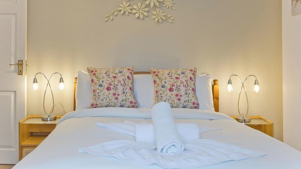 A neatly made bed with floral pillows, two bedside lamps, and a wall decoration.
