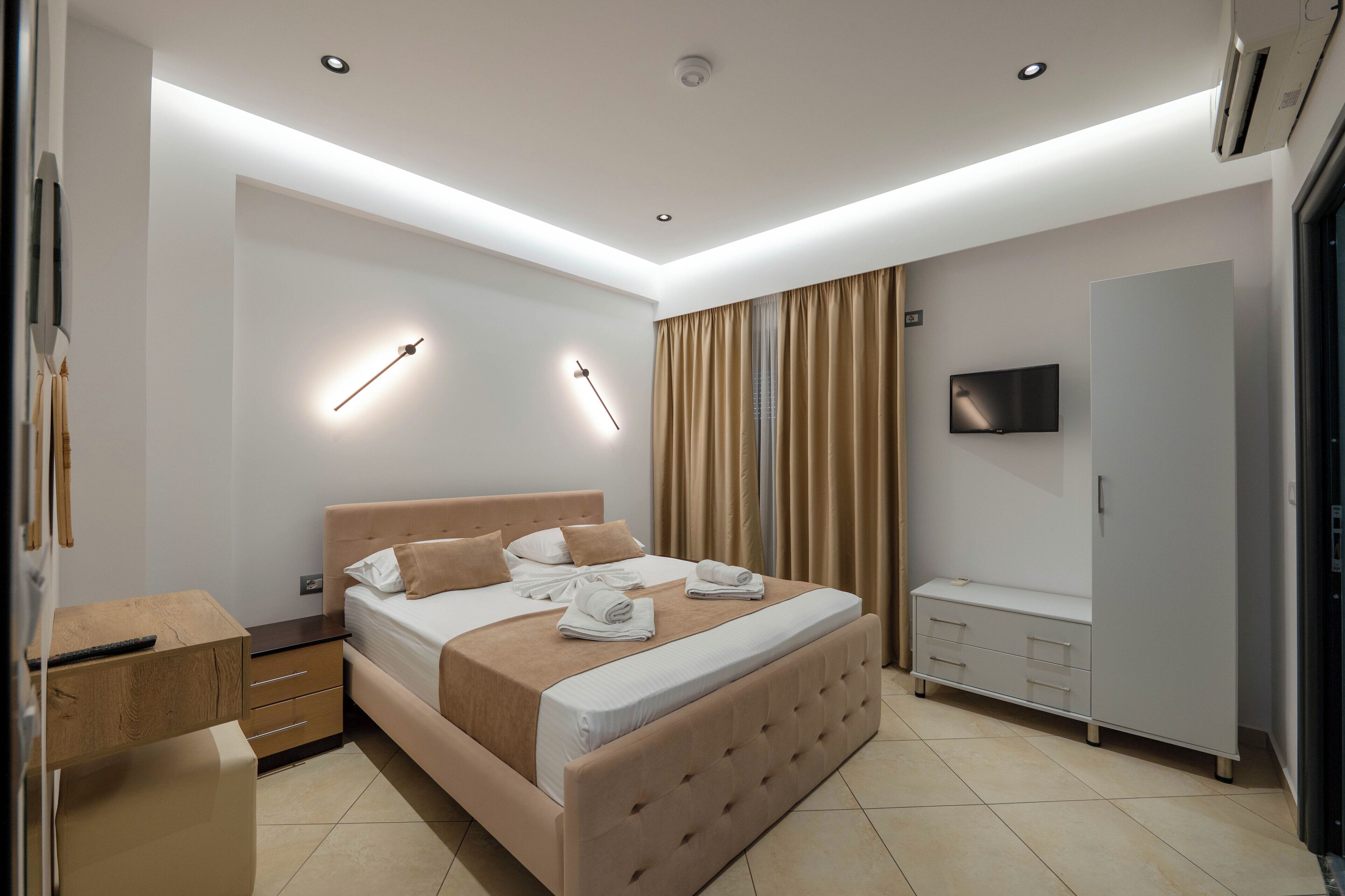 A modern bedroom with a large bed, bedside tables, a wardrobe, and a flat-screen TV.