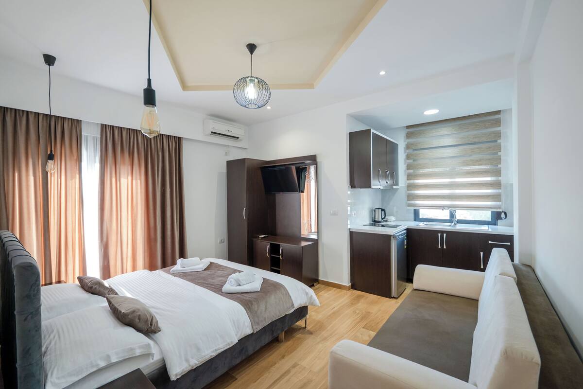 Una habitación de hotel moderna con una cama, un sofá, una kitchenette y un televisor.