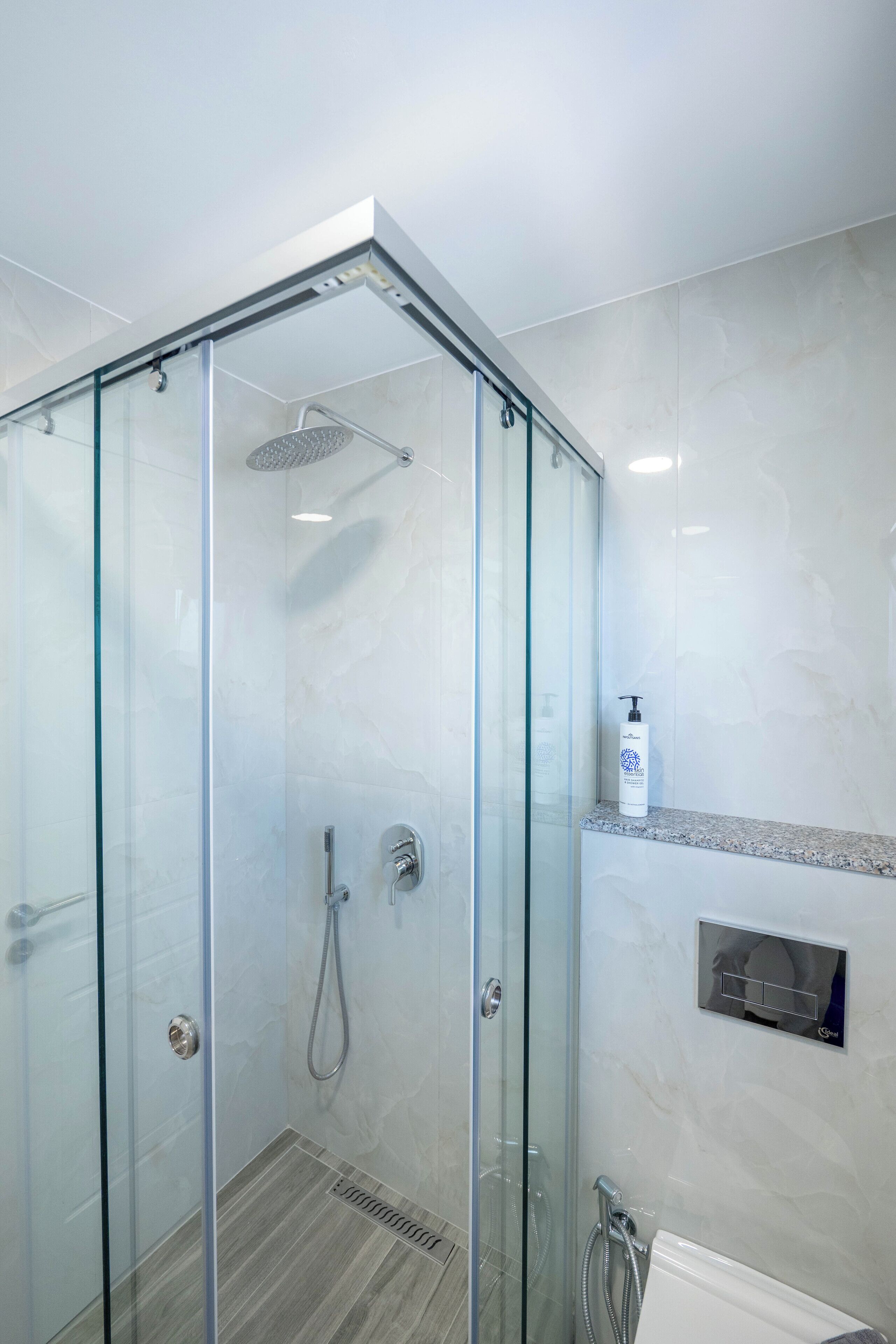 A modern shower enclosure with a glass door, a handheld showerhead, and a wall-mounted control panel.