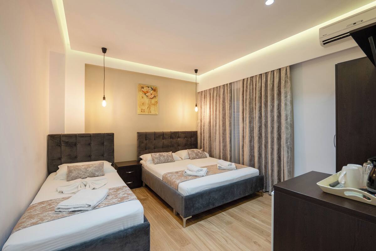 Habitación de hotel con dos camas, un espejo grande, un escritorio y una bandeja con alimentos para el desayuno, además de un equipo de aire acondicionado.