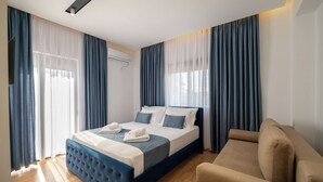 A modern hotel room with a large bed, a sofa, and a window with curtains. - Villa JIOTA (Ksamil)
