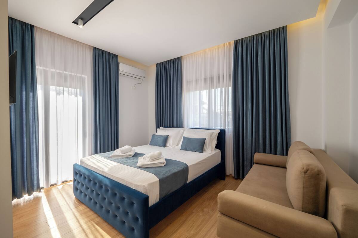 Una habitación de hotel moderna con una cama grande, un sofá y una ventana con cortinas.