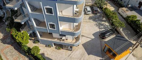 A multi-story building with balconies, a sign reading "Villa Jiota," and a parking area with cars.