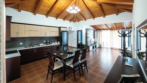 A spacious kitchen with wooden beams, a dining area with a table and chairs, and a large window with curtains. - Villa JIOTA (Ksamil)