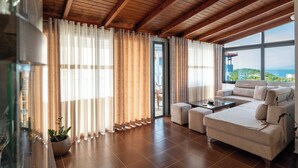 A spacious living room with a wooden ceiling, large windows, a sofa, and a coffee table. - Villa JIOTA (Ksamil)