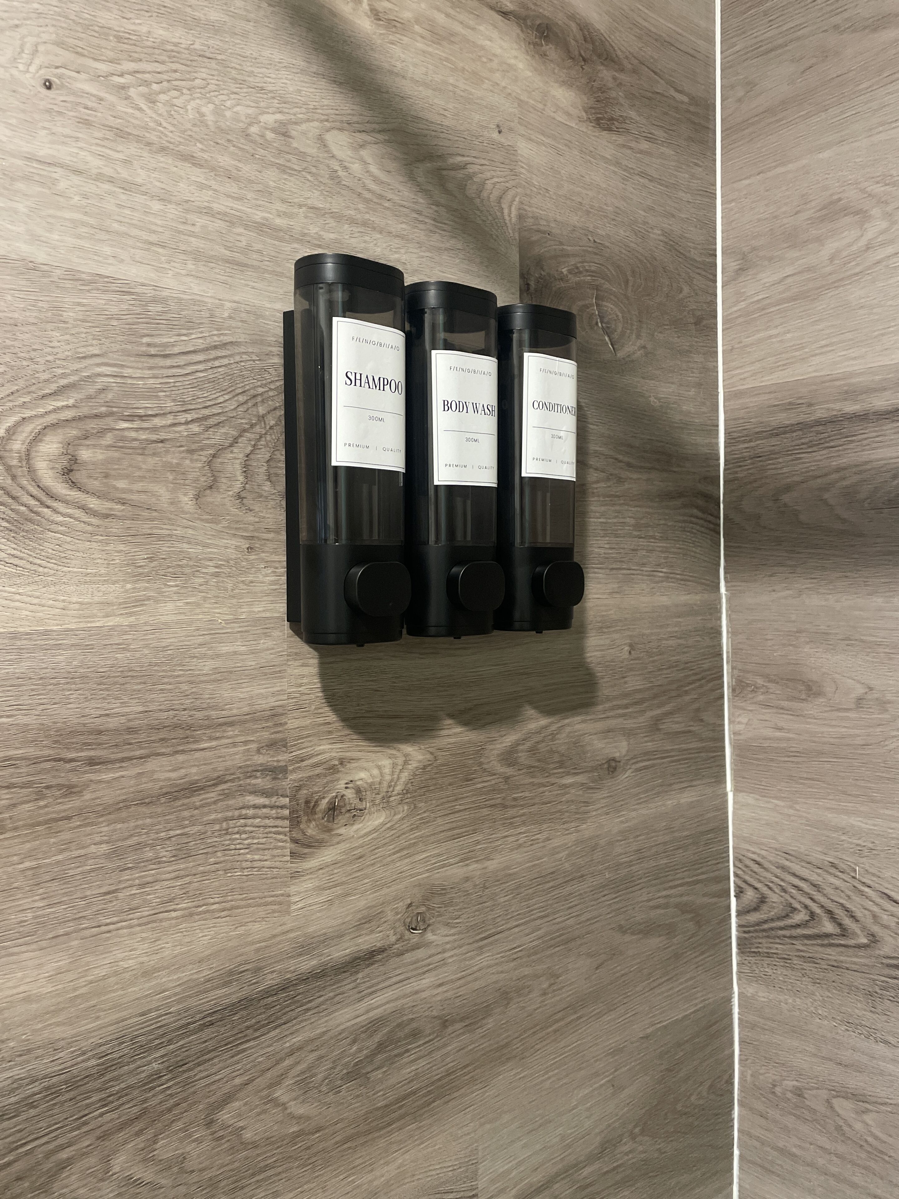 Three black bottles of shampoo, body wash, and conditioner on a wooden surface.