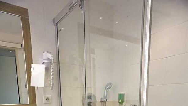 Un baño moderno con cabina de ducha de vidrio, lavabo con espejo y un cubo de basura.