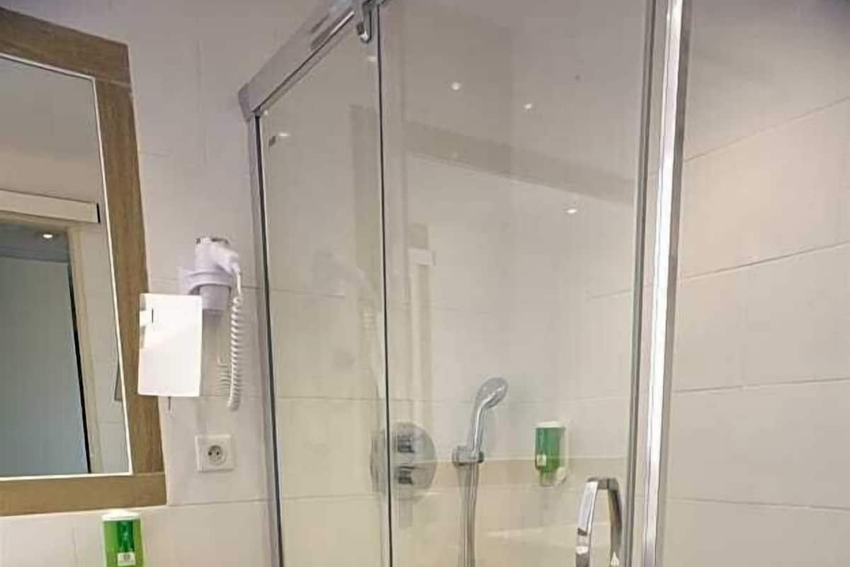 A modern bathroom with a glass-enclosed shower, a sink with a mirror, and a trash bin.