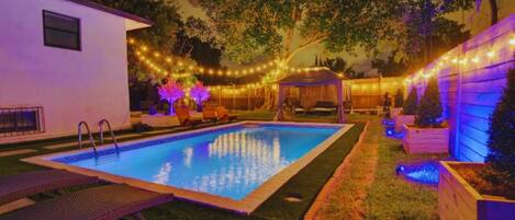 Relax by the pool surrounded by a lush garden and a pergola with twinkling lights.