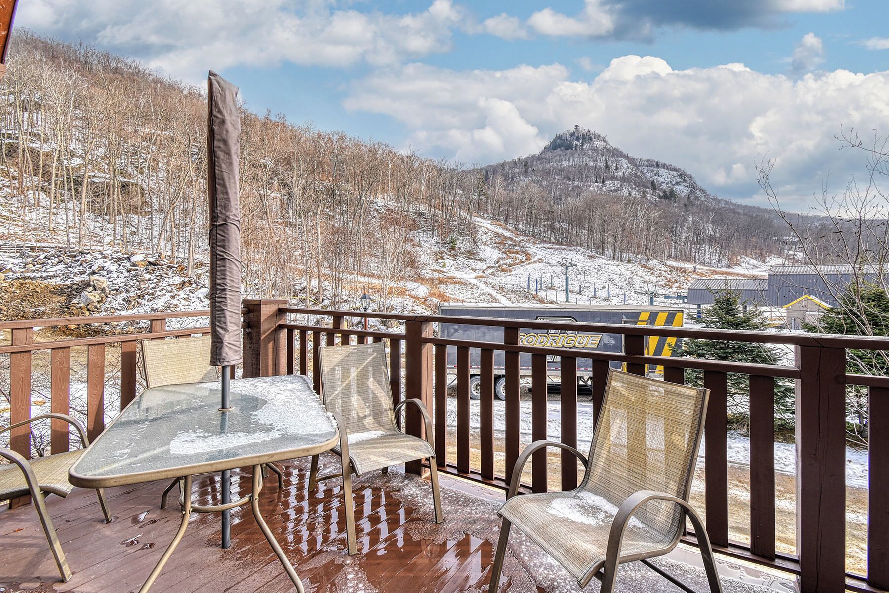 A wooden deck with a glass table and chairs, overlooking a snowy mountain landscape.