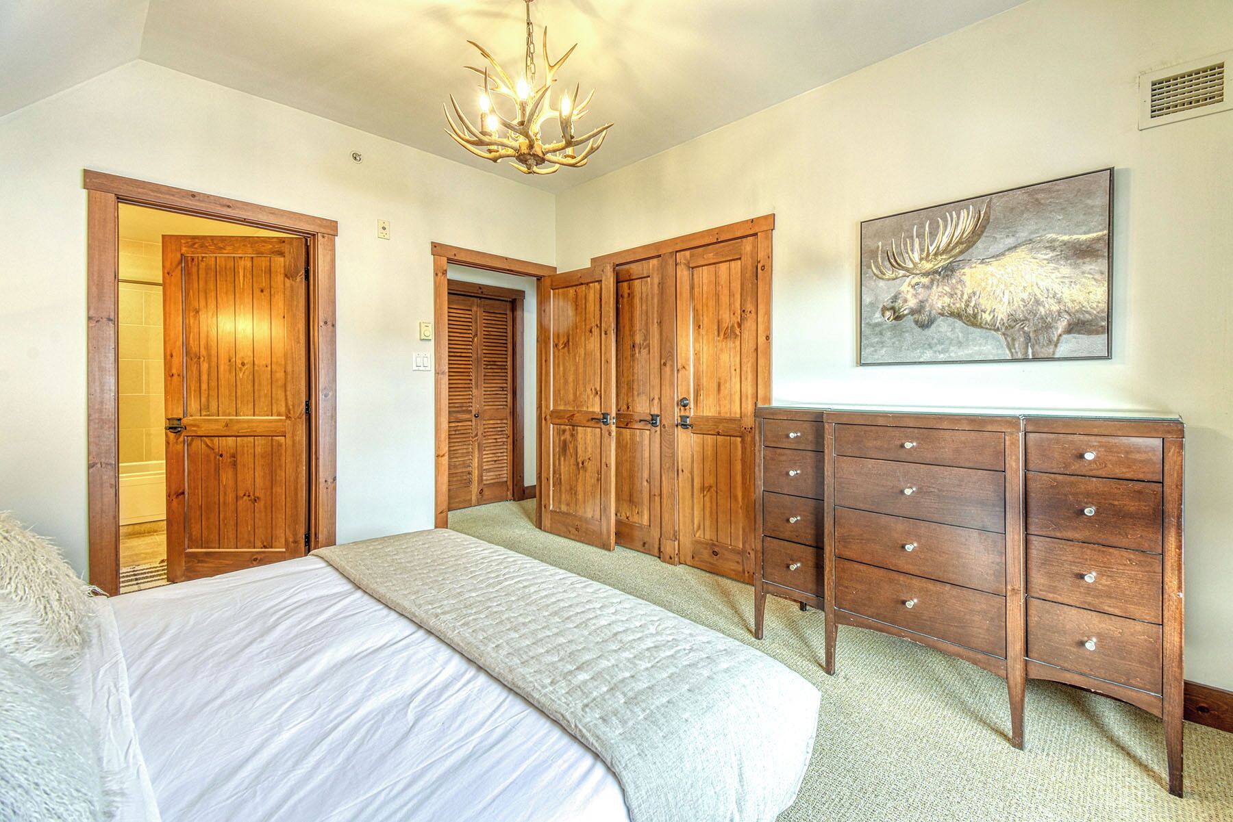A bedroom with a bed, wooden wardrobe, and a chandelier.