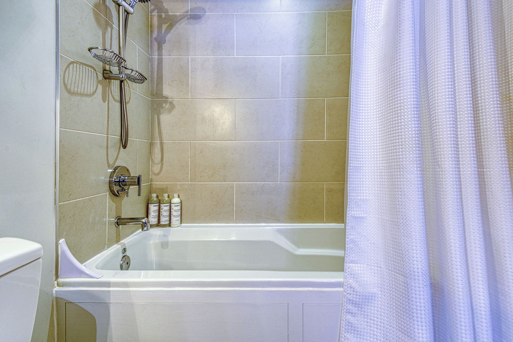 A bathroom with a bathtub, a shower, and a toilet. There are toiletries on the wall.