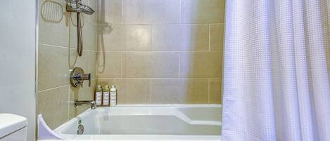 A bathroom with a bathtub, a shower, and a toilet. There are toiletries on the wall.