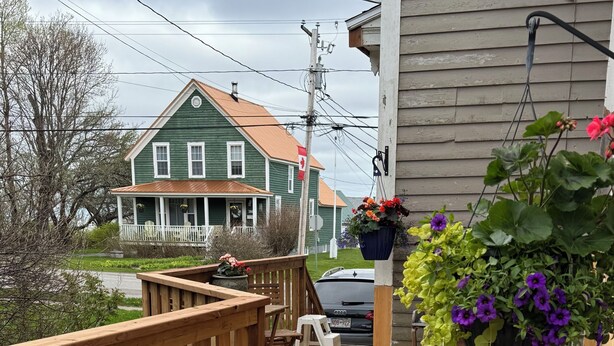A wooden deck with a railing, a small table, and chairs. There are hanging flower baskets with purple flowers. - Welcome to Victorian by the bay
Built in 1830 the oldest home in the village (Saint Martins)