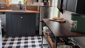 A modern kitchen with dark cabinets, a checkered floor, a hanging light fixture, and a window with a view. - Welcome to Victorian by the bay
Built in 1830 the oldest home in the village (Saint Martins)