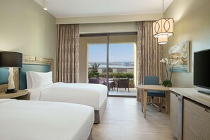 A hotel room with two beds, a desk, a TV, and a balcony with a view. - Hilton Dead Sea Resort & Spa (Sweimeh)