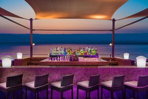 A bar with a view of the sea, bar stools, and a variety of bottles. - Hilton Dead Sea Resort & Spa (Sweimeh)