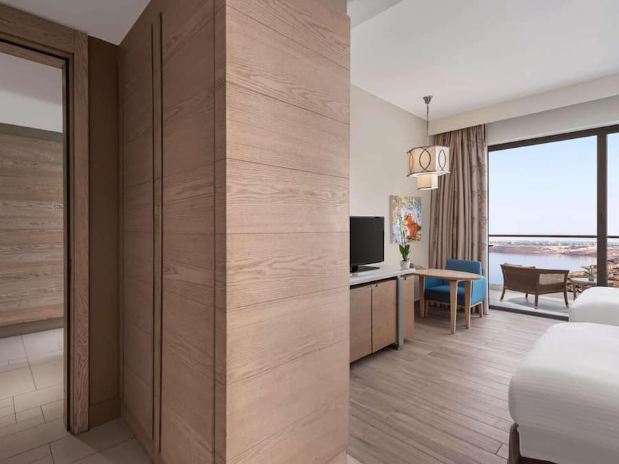 A modern hotel room with a large window, a flat-screen TV, a desk, and a bed.