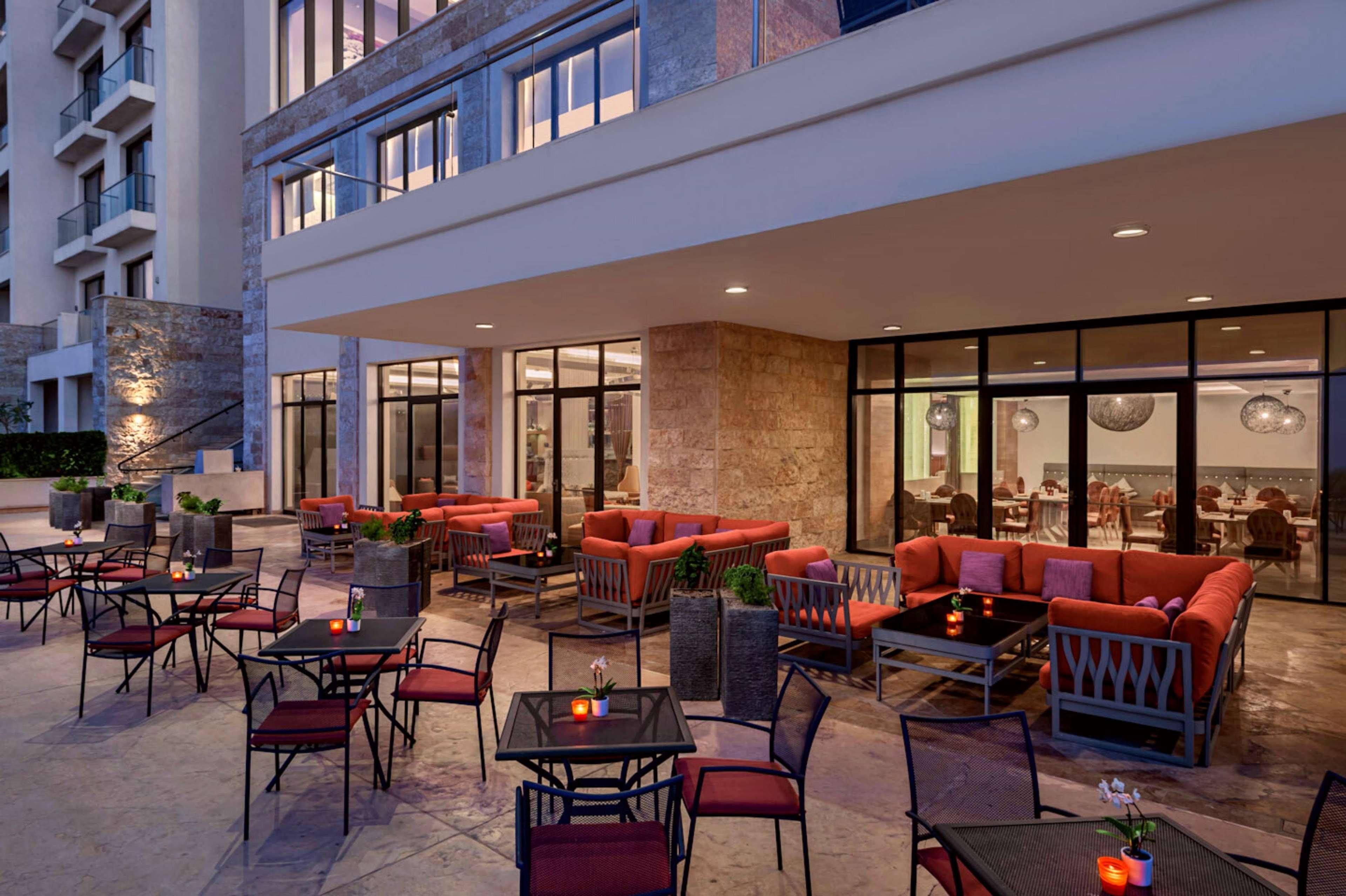 An outdoor seating area with tables and chairs, a large red sofa, and a glass-enclosed dining area.