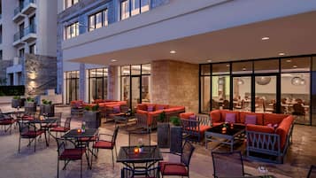 An outdoor seating area with tables and chairs, a large red sofa, and a glass-enclosed dining area.
