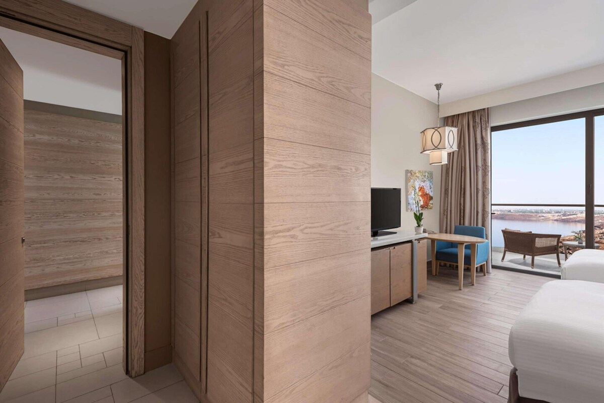 A modern hotel room with a large window, a flat-screen TV, a desk, and a bed.