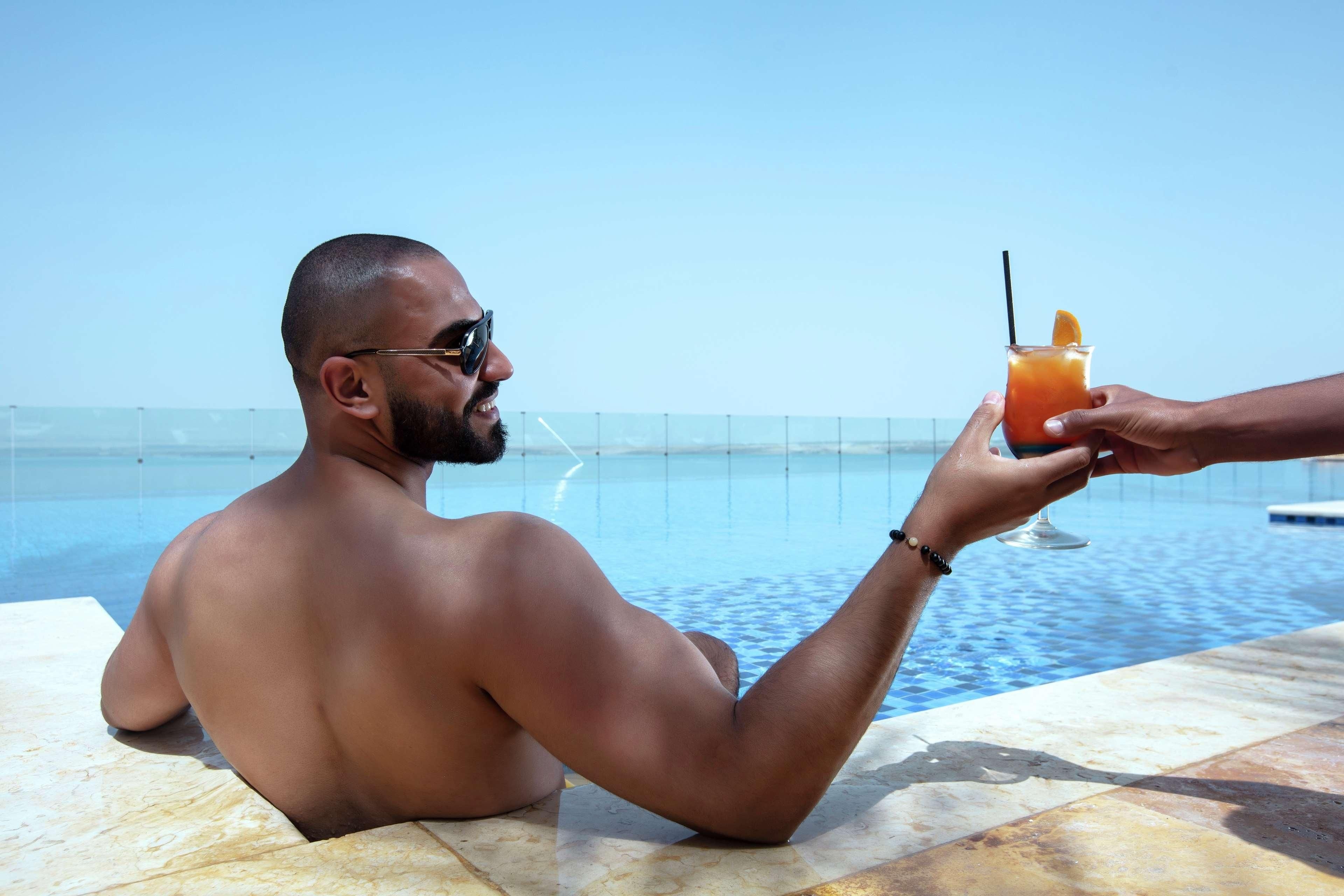 A person sitting by a pool with a drink in hand.