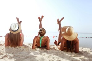 Trois personnes sont assises sur une plage de sable, face à l’eau.