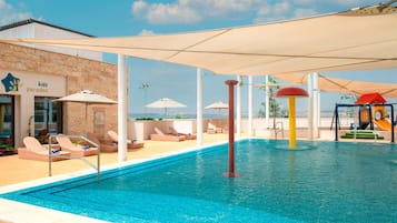 Una piscina con sillones de descanso y sombrillas, una zona de juegos para niños y un edificio con un letrero que dice 'kidz paradise'.