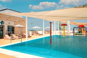 A swimming pool with lounge chairs and umbrellas, a children's play area, and a building with a sign reading 'kidz paradise'. - Hilton Dead Sea Resort & Spa (Sweimeh)