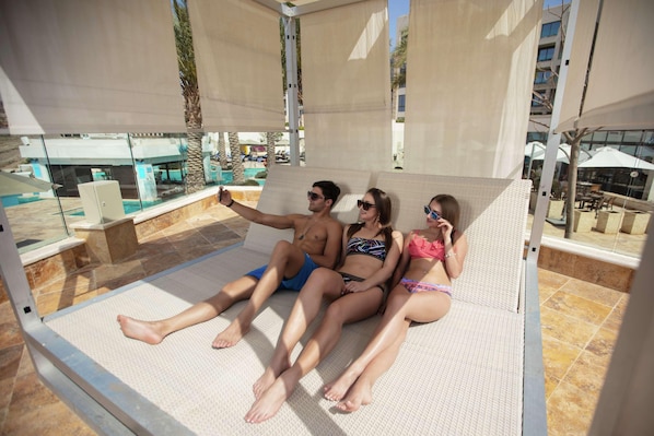 A couple and a child relaxing on a sunbed with a pool view. - Hilton Dead Sea Resort & Spa (Sweimeh)