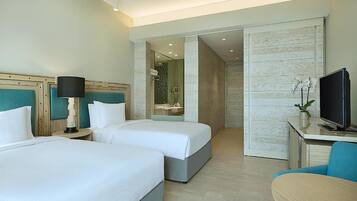 A hotel room with two beds, a desk with a television, and a bathroom with a shower and sink.