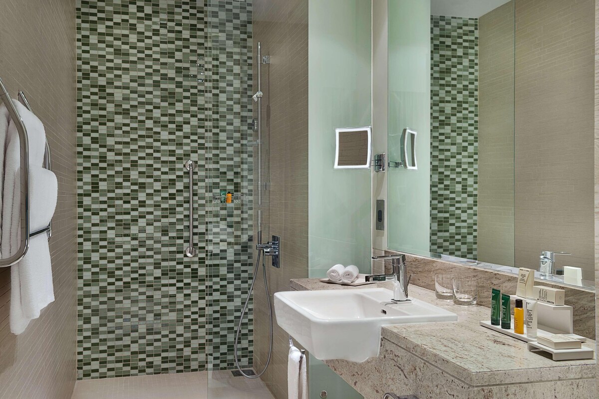 A modern bathroom with a glass-enclosed shower, a sink with toiletries, and a large mirror.