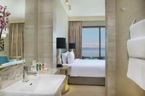 A hotel room with a large bed, a bathroom with a sink and mirror, and a view of the mountains. - Hilton Dead Sea Resort & Spa (Sweimeh)