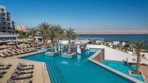A pool area with lounge chairs, palm trees, and a view of the sea. - Hilton Dead Sea Resort & Spa (Sweimeh)