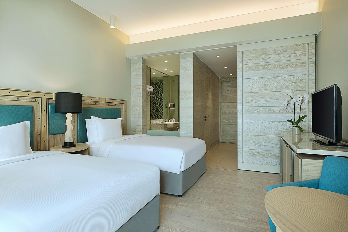 A hotel room with two beds, a desk with a television, and a bathroom visible through an open door.