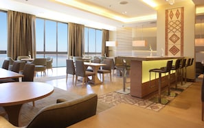 A hotel lobby with a bar, seating area, and large windows. - Hilton Dead Sea Resort & Spa (Sweimeh)