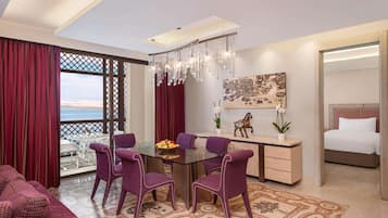 A modern hotel room with a balcony, a dining area with purple chairs, a bed, and a decorative wall piece.