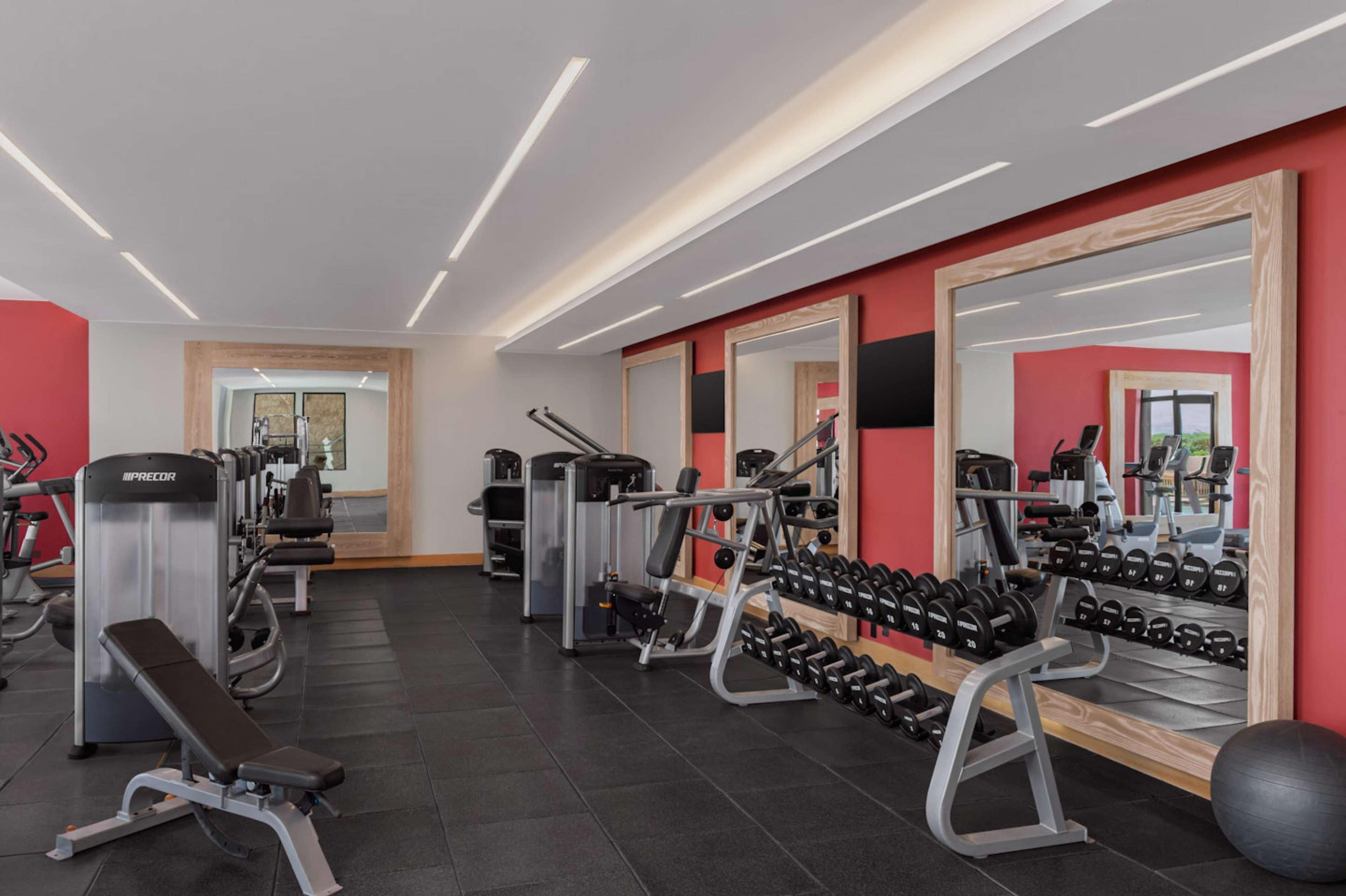 A gym with exercise equipment, mirrors, and a wall-mounted dumbbell rack.