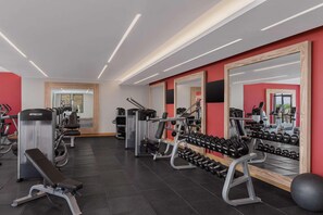 A gym with exercise equipment, mirrors, and a wall-mounted dumbbell rack.