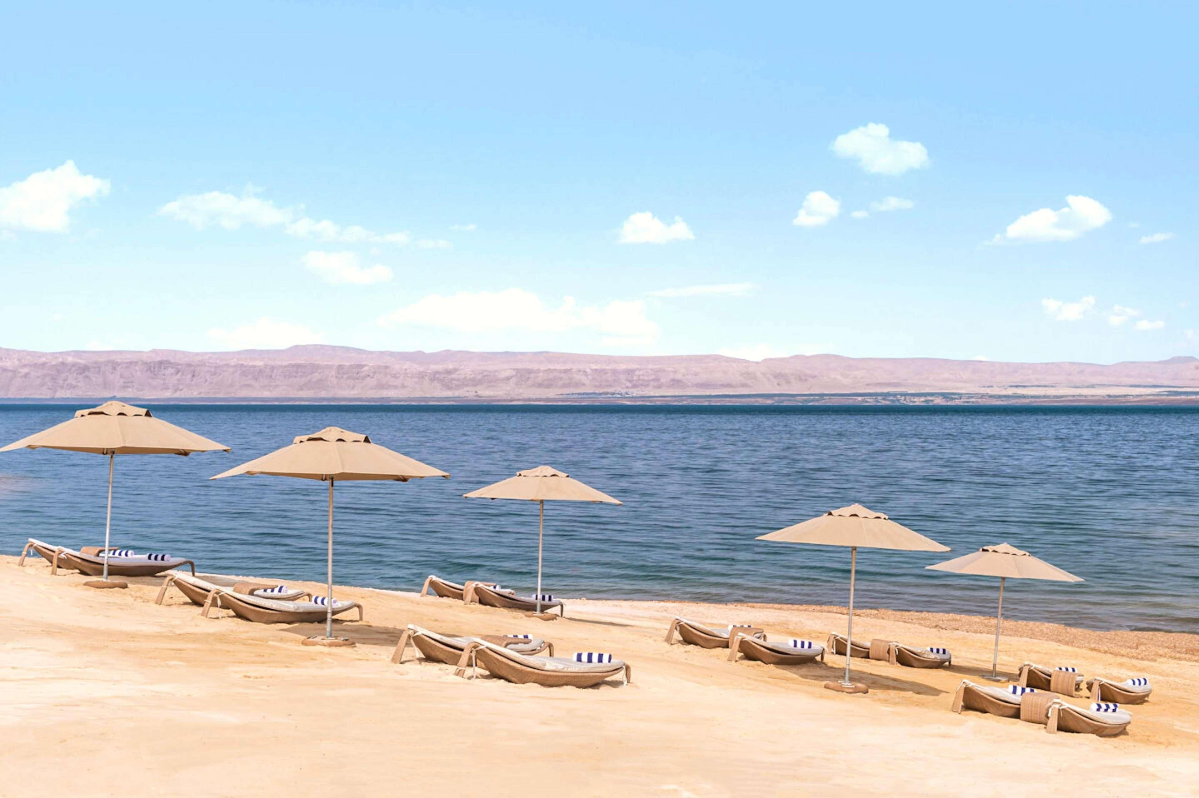 A beach with lounge chairs and umbrellas, a calm sea, and distant mountains.