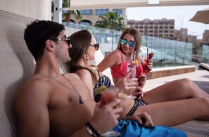 A poolside setting with reclining chairs, a glass railing, and a view of buildings in the background. - Hilton Dead Sea Resort & Spa (Sweimeh)