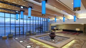 A spacious lobby with a large window overlooking a body of water, a central decorative vase, and modern lighting fixtures. - Hilton Dead Sea Resort & Spa (Sweimeh)