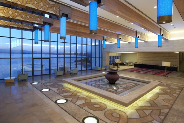 A spacious lobby with a large window overlooking a body of water, a central decorative vase, and modern lighting fixtures. - Hilton Dead Sea Resort & Spa (Sweimeh)