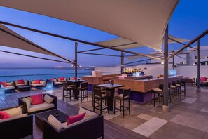 A rooftop bar with outdoor seating, a bar counter, and a view of the sea. - Hilton Dead Sea Resort & Spa (Sweimeh)